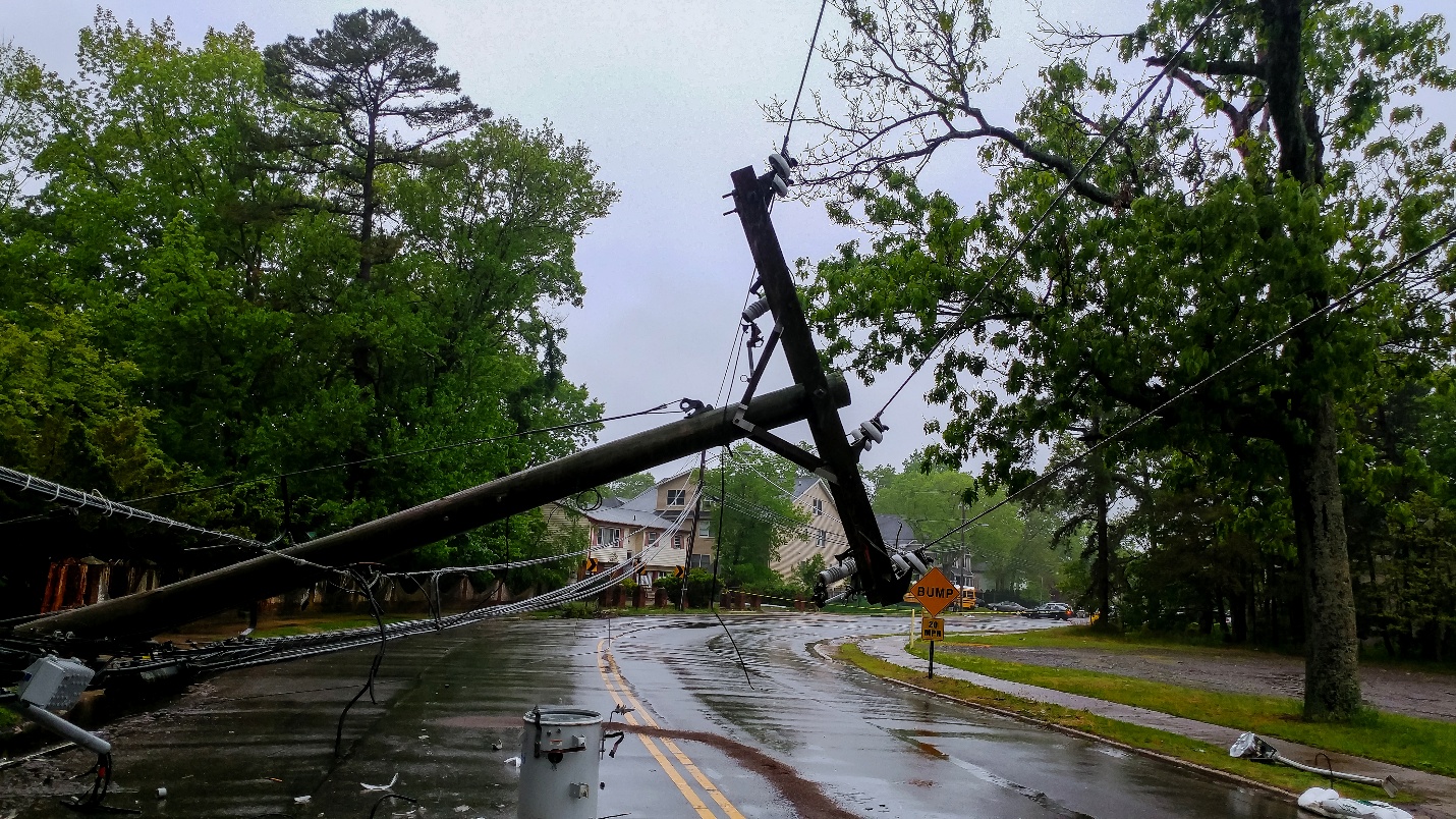A downed power pole lies across a rain-soaked street, with water pooling around its base