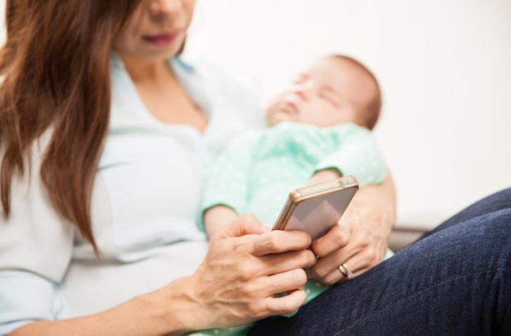 A mother reading through her phone with her baby on hands